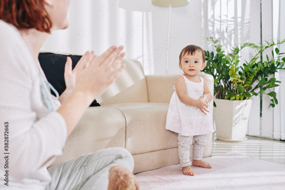 Mother applauding to her dancing little baby girl when they are staying home due to pandemic
