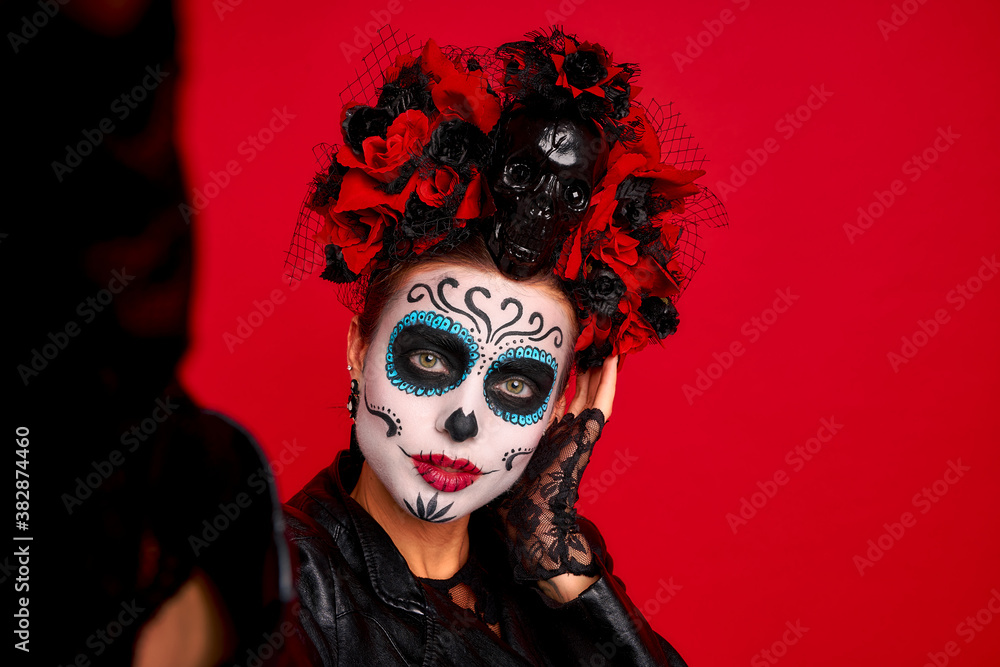 Closeup photo of funny folklore witch creature character death day facial creepy makeup masquerade. Sugar skull girl take selfies wear floral headwear amd lether jaket isolated on red background