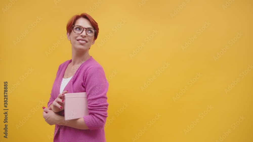 Mature red haired woman over isolated yellow background looking up while smiling. Mature red haired woman over isolated yellow background looking up while smiling.