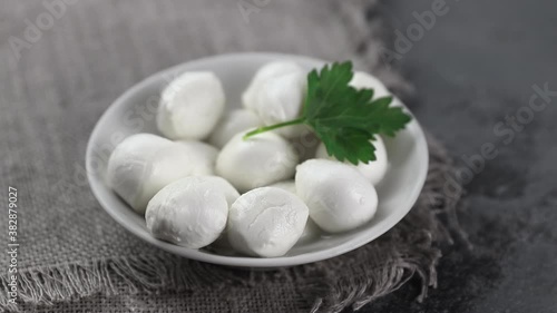 placing with metal spoon round pieces of mozarella cheese on a white plate against dark gray background, side view
