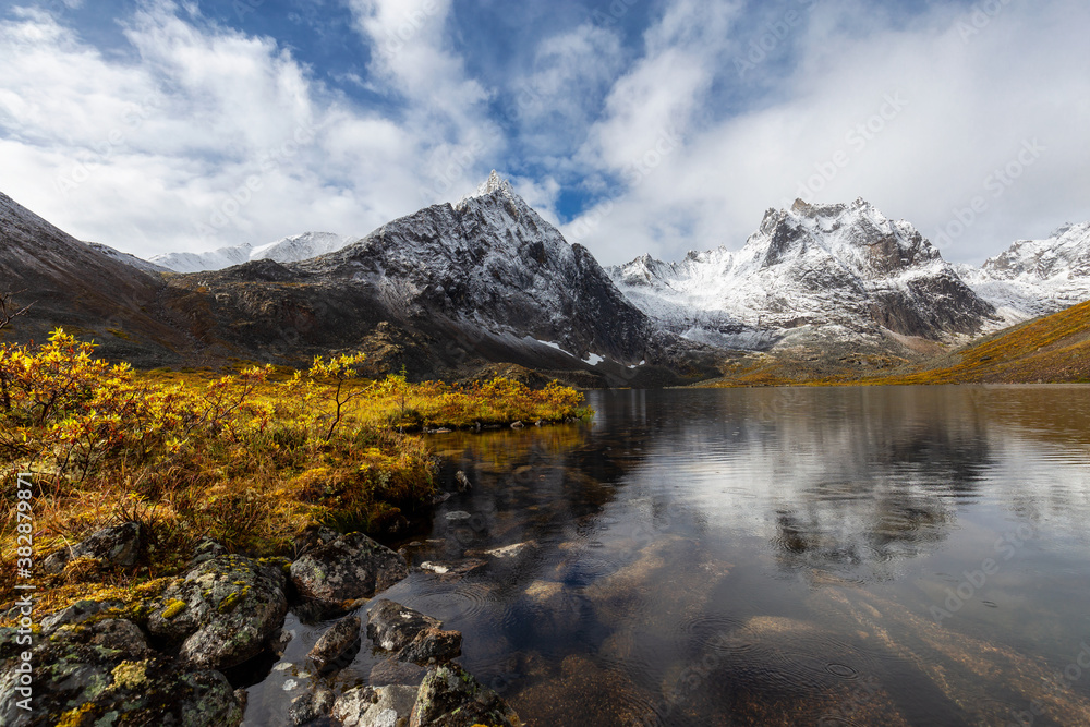 Beautiful View of Scenic Alpine Lake, Rocks and Snowy Mountain Peaks in Canadian Nature. Season change from Fall to Winter. Taken at Grizzly Lake in Tombstone Territorial Park, Yukon, Canada.