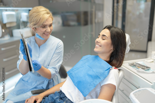 Female dentist showing female patient a tablet pc with treatment information with chromakey on the screen