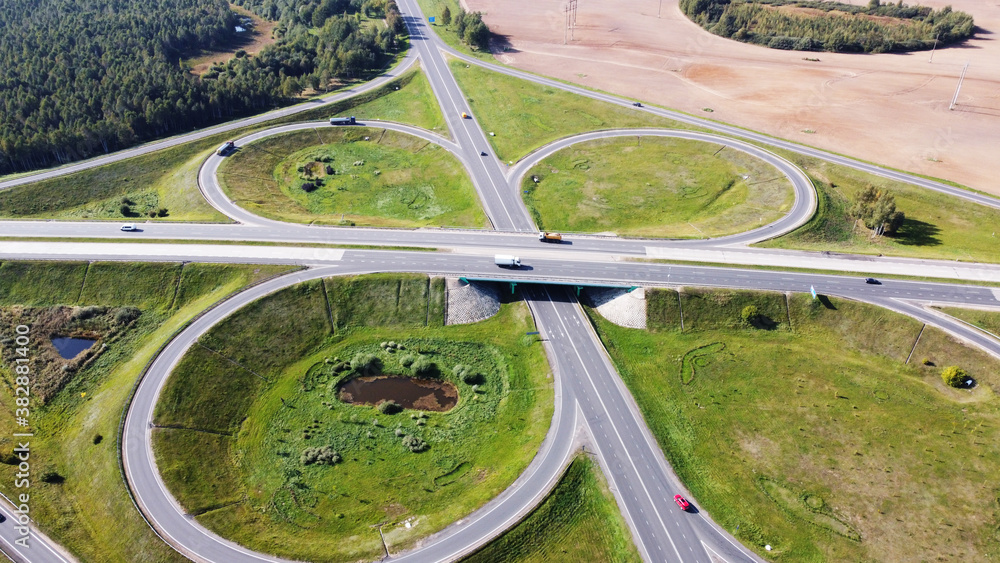 Top view of highway with intersection and roundabout in the middle of fields on a sunny day