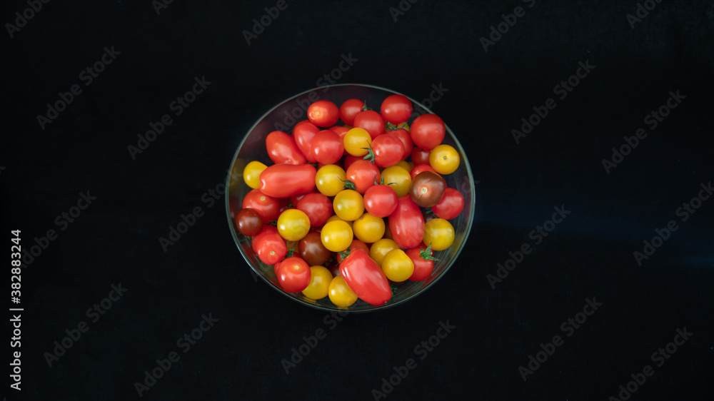 Small cocktail tomatoes, multicolored, round and oval, in a transparent glass container, on black background, close-up
Small cocktail tomatoes, multicolored, round and oval, in a transparent glass container, on black background, close-up