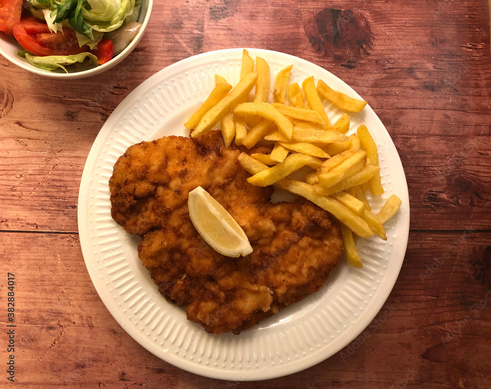 Wiener Schnitzel with french fries and lemon. Viennese breaded Escalope, coated in flour, egg and breadcrumbs, then deep fried to golden brown and served with french fries, salad and lemon. Wiener Schnitzel with french fries and lemon. Viennese breaded Escalope, coated in flour, egg and breadcrumbs, then deep fried to golden brown and served with french fries, salad and lemon.
