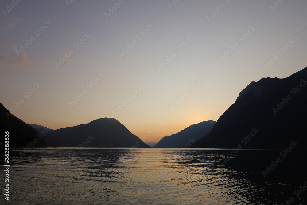 Colorful sunset in Italy over a mountain range with still lake in foreground during golden hour in late summer