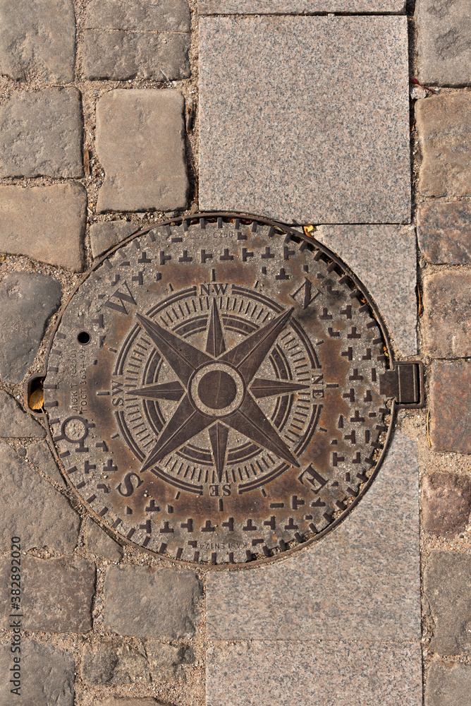 Sewer manhole on the sidewalk indicating the cardinal directions.