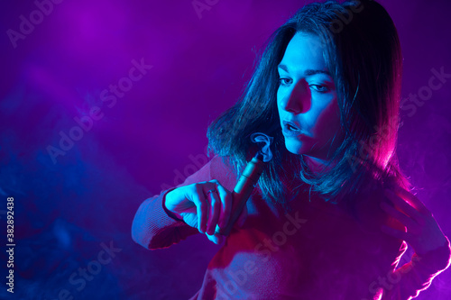 A long-haired girl with a VAPE on a lilac background. Smoking electronic cigarettes. The concept of vaping. A thoughtful girl with an e-cigarette in her hands.