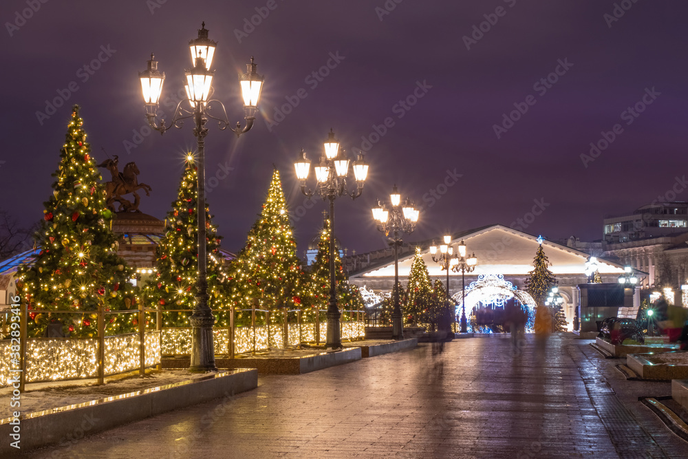 Moscow. Russia. Festive evening on Manezhnaya square. Decorated Christmas trees in the center of Moscow. Waiting for the holiday. The light of lanterns and garlands against the dark sky.
