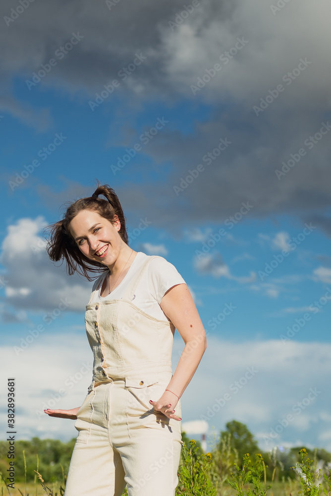 Happy girl against the blue sky in a beige jumpsuit.