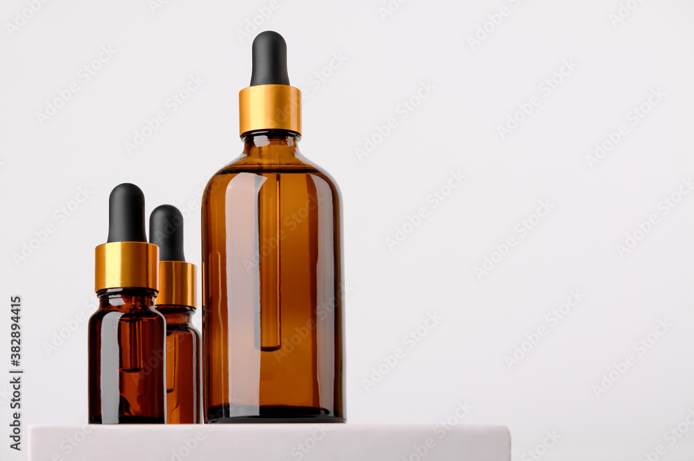 Set of brown glass bottles with essential oil on a white background on a stand. Packaging of a beauty product with a pipette for alternative medicine treatment. Aromatherapy, homeopathy. Copy space