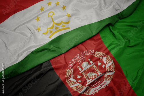 waving colorful flag of afghanistan and national flag of tajikistan. macro
