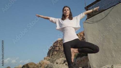 Young woman practising yoga on sunny day on the rocky sea coast.Tree posture. High quality photo photo