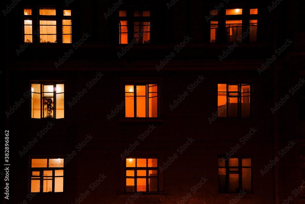 nine windows of an apartment building lit by electric light in the dark of night