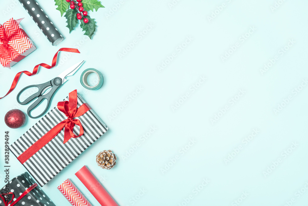 Gift boxes wrapped in black and white striped and red paper with wrapping materials over a blue background. Christmas presents preparation. Copy space.