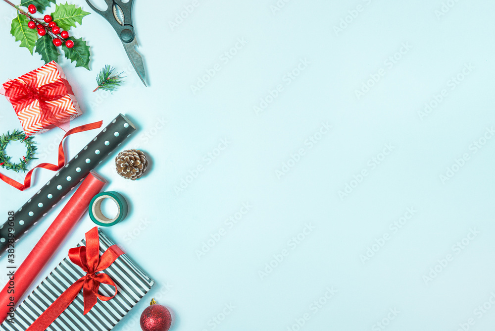 Gift boxes wrapped in black and white striped and red paper with wrapping materials over a blue background. Christmas presents preparation. Copy space.