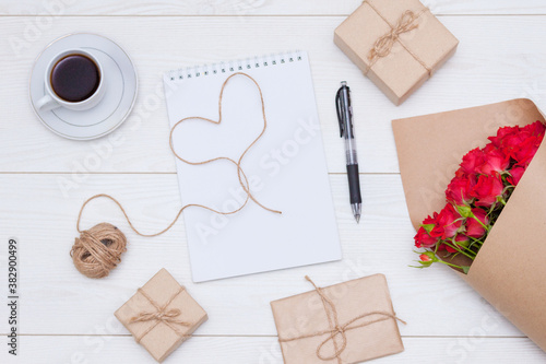 Flat lay composition. Cup of coffee, red rosses, gift boxes, notebook. Natural materials concept.
