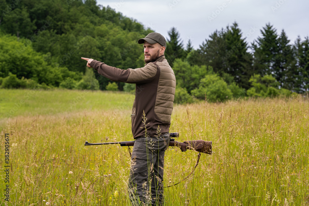 Young hunter pointing a direction with his hand while holding a sniper rifle Young hunter pointing a direction with his hand while holding a sniper rifle