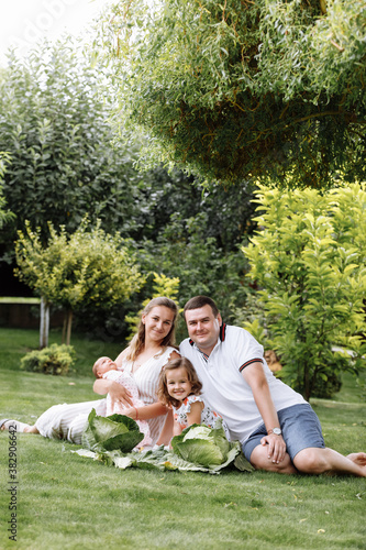 father, mother and two children, baby girl and little daughter on the grass with cabbages on summer day. Happy family sitting together outdoors, having fun. Happiness and harmony in family life.