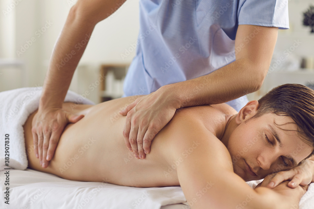 Fototapeta premium Relaxed young man enjoying therapeutic body massage done by professional masseur