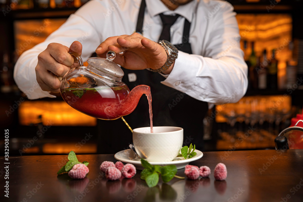 A male bartender pours hot tea at the bar in a restaurant
A male bartender pours hot tea at the bar in a restaurant