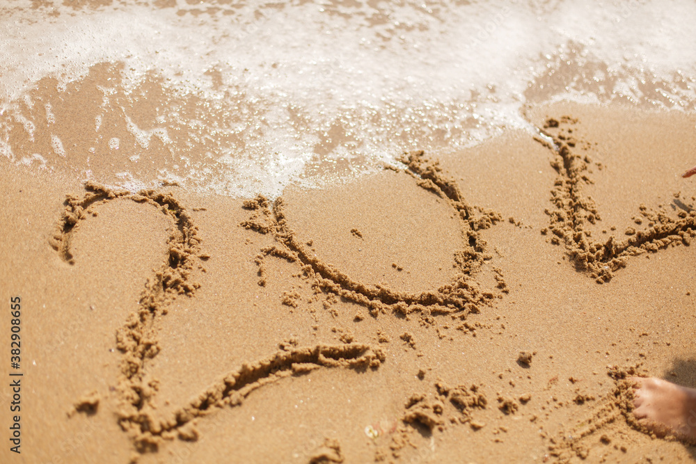Person writing 2020 sign on sandy beach and wave foam covering and erasing 2020 inscription Person writing 2020 sign on sandy beach and wave foam covering and erasing 2020 inscription