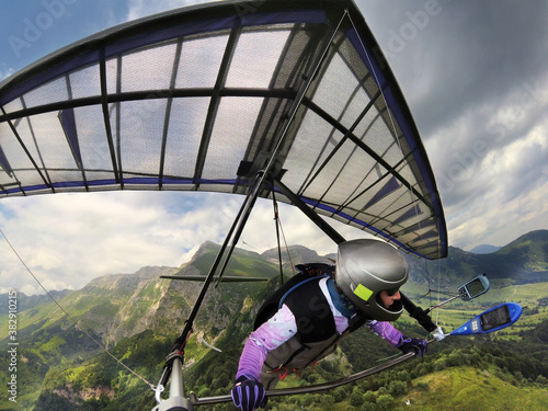 Hang glider pilot soars high above mountain peaks.