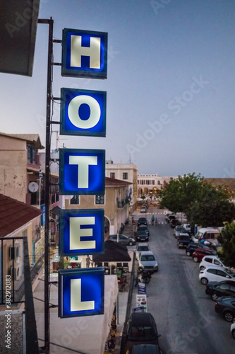 Lit blue neon hotel sign overlooking a crowded street below in the greek island.