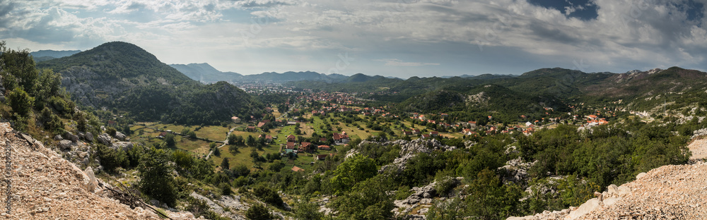 Panorama of Cetinje, former capital city of Montenegro. View towards the houses of cetinje hiding in lush green hills and forests. Some rocks in the foreground.
