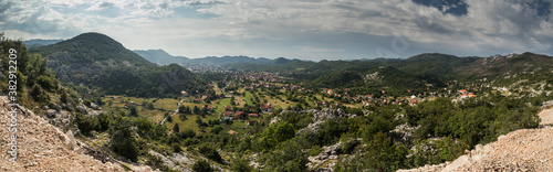 Panorama of Cetinje  former capital city of Montenegro. View towards the houses of cetinje hiding in lush green hills and forests. Some rocks in the foreground.