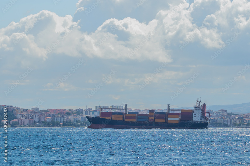 Fototapeta premium A big container cargo ship or carrier traveling through the Dardanele strait in Turkey on a cloudy day. Heavy loaded container ship with colorful containers.