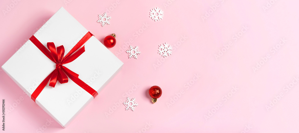 Luxury white gift box with red ribbon and snowflakes on pink background with copy space isilated flat lay. Minimalist composition. Winter holidays concept Christmas, New Year, birthday, discounts.