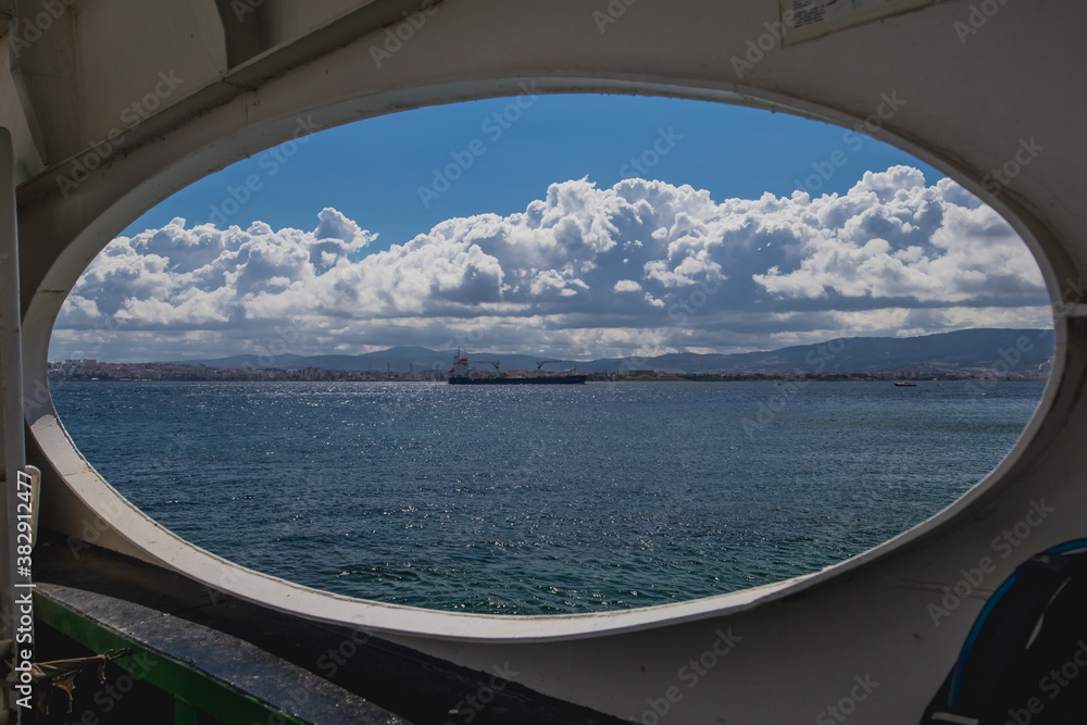 A big cargo ship or carrier traveling through the Dardanele strait in Turkey on a cloudy day, looking through a window of a ferry going towards Canakkale.