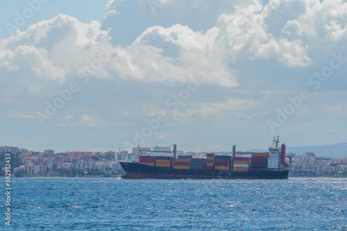 A big container cargo ship or carrier traveling through the Dardanele strait in Turkey on a cloudy day. Heavy loaded container ship with colorful containers.