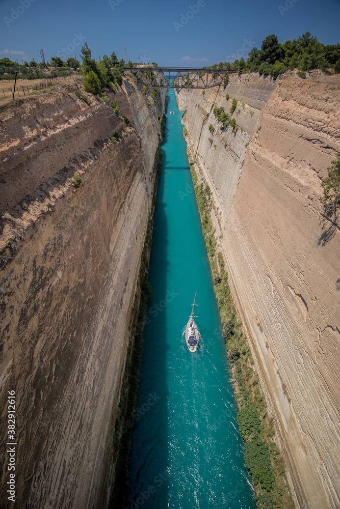 Corinth or corinthian canal in Greece. A narrow waterway that connects Ionic sea with Aegean sea. Narrow water passage carved in rock on a sunny day.