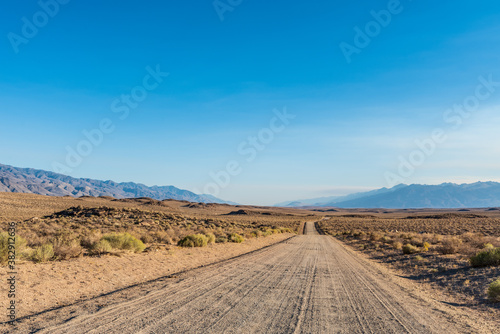 dirt road in desert valley heading toward distant mountains in California 