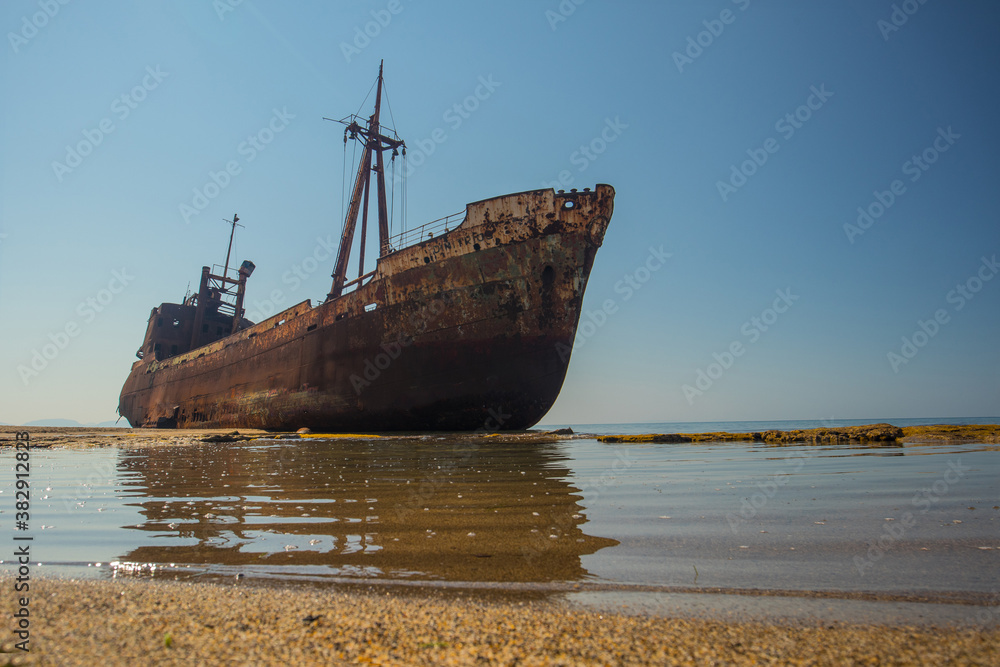 Dimitrios shipwreck in  Gythio, Greece. A partially sunken rusty and metal shipwreck decaying through time on a sandy beach on a sunny day. Famous shipwreck in greece.