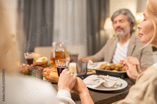 Hands of family members saying thanks to Lord in Thanksgiving prayer by table