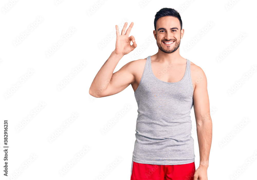 Young handsome man wearing swimwear and sleeveless t-shirt smiling positive doing ok sign with hand and fingers. successful expression.