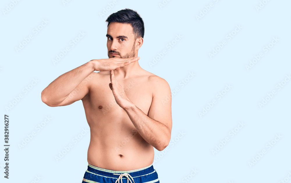 Young handsome man wearing swimwear doing time out gesture with hands, frustrated and serious face