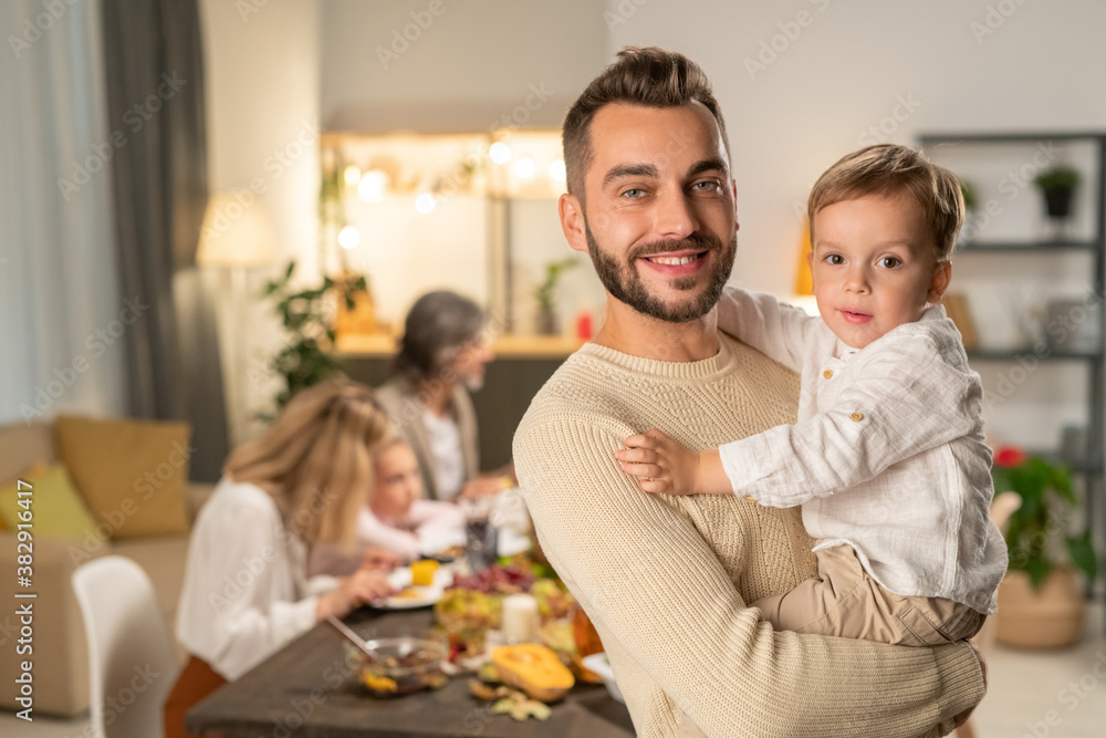 Happy young father with his cute little son on hands standing in front of camera Happy young father with his cute little son on hands standing in front of camera