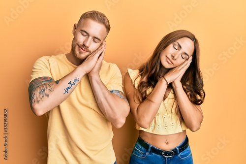 Young couple of girlfriend and boyfriend hugging and standing together sleeping tired dreaming and posing with hands together while smiling with closed eyes.