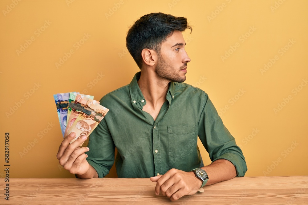 Young handsome man holding canadian dollars looking to side, relax profile pose with natural face and confident smile. Young handsome man holding canadian dollars looking to side, relax profile pose with natural face and confident smile.