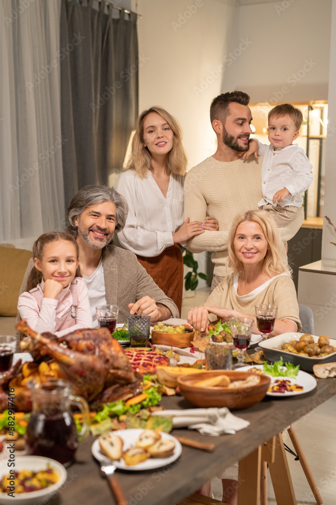 Large family of three generations sitting by table served by variety of food