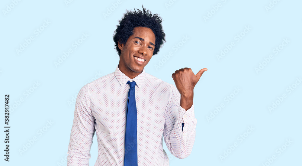 Handsome african american man with afro hair wearing business clothes smiling with happy face looking and pointing to the side with thumb up. Handsome african american man with afro hair wearing business clothes smiling with happy face looking and pointing to the side with thumb up.