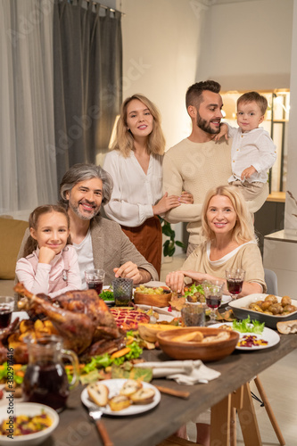 Large family of three generations sitting by table served by variety of food