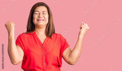 Middle age latin woman wearing casual clothes very happy and excited doing winner gesture with arms raised, smiling and screaming for success. celebration concept.