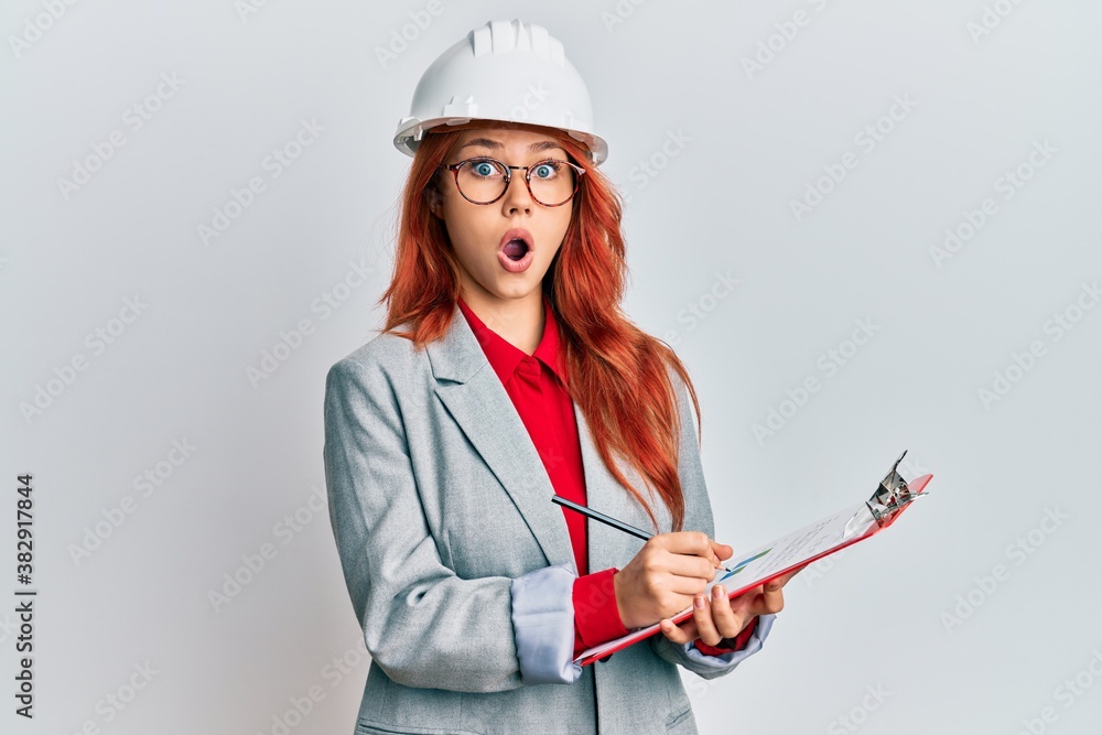 Young redhead woman wearing architect hardhat afraid and shocked with surprise and amazed expression, fear and excited face. Young redhead woman wearing architect hardhat afraid and shocked with surprise and amazed expression, fear and excited face.