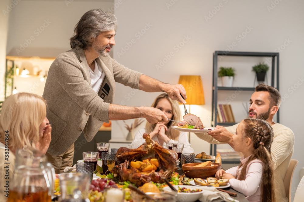 Mature man with knife and fork giving slice of roasted turkey to young male