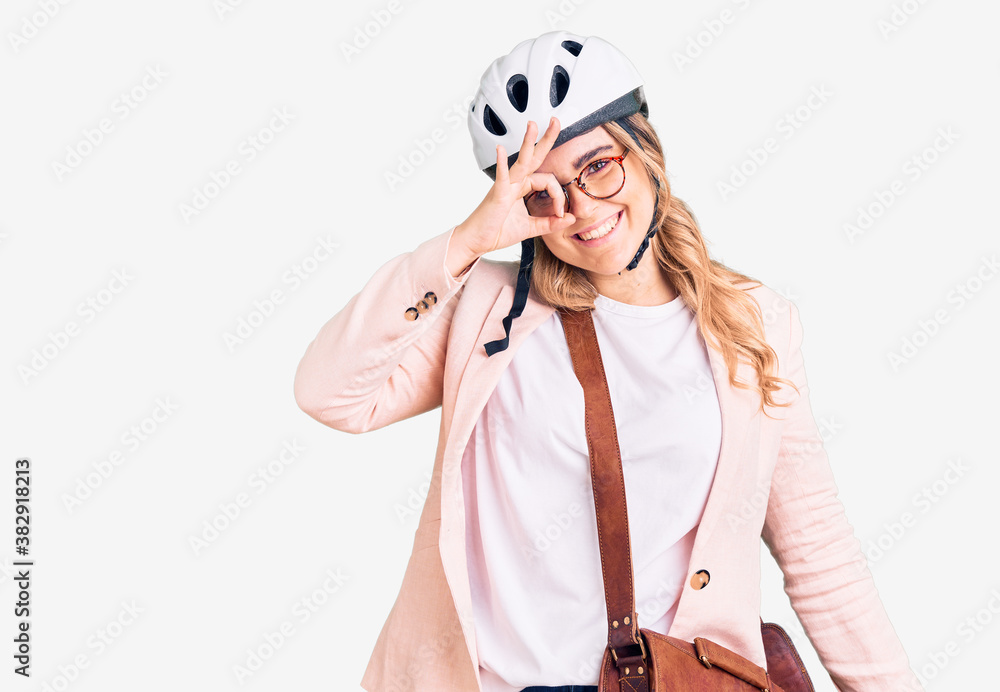Young caucasian woman wearing bike helmet and leather bag smiling happy doing ok sign with hand on eye looking through fingers Young caucasian woman wearing bike helmet and leather bag smiling happy doing ok sign with hand on eye looking through fingers